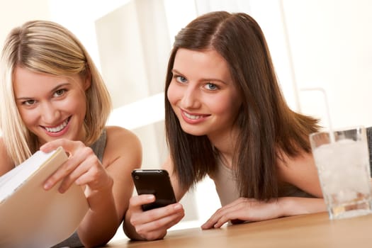 Two smiling students enjoying free time with book and mobile phone