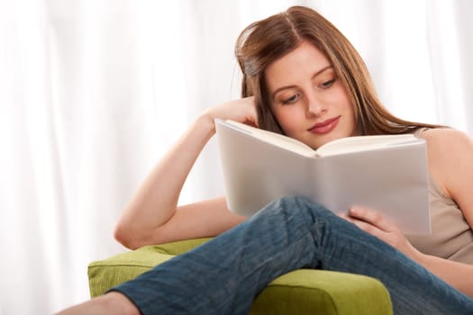 Young brunette reading book, sitting on green armchair