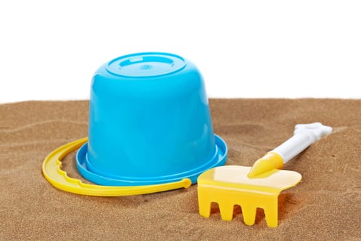 Bucket full and rake on the sand with copy space on a white background. Shallow depth of field