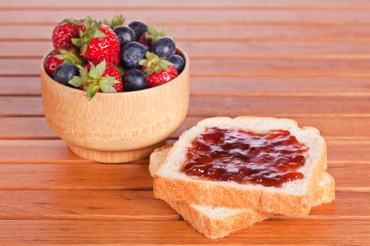 Two toast with jam, blueberries and strawberries in a bowl on wooden background. Shallow depth of field
