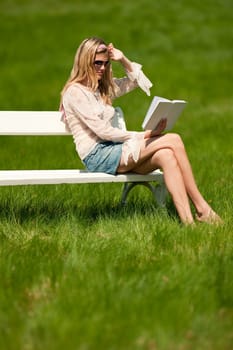 Spring and summer - Young woman relaxing in meadow on white bench on sunny day