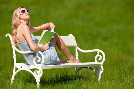 Spring and summer - Young woman relaxing in meadow on white bench on sunny day enjoying sun