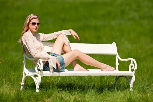 Spring and summer - Young woman relaxing in meadow on white bench on sunny day