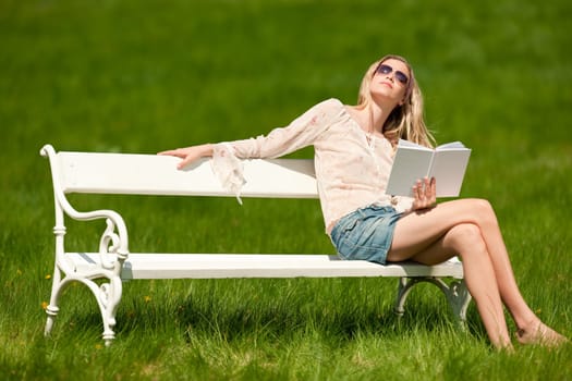 Spring and summer - Young woman relaxing in meadow on white bench on sunny day
