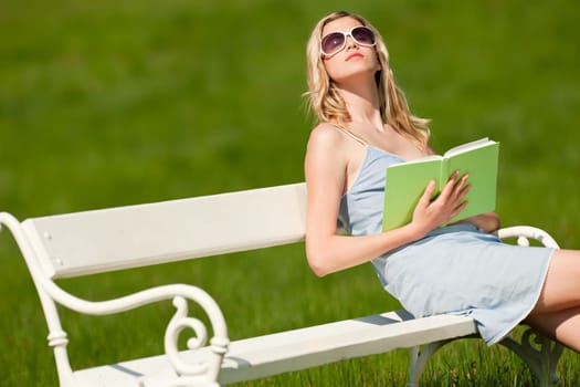 Spring and summer - Young woman relaxing in meadow on white bench on sunny day enjoying sun
