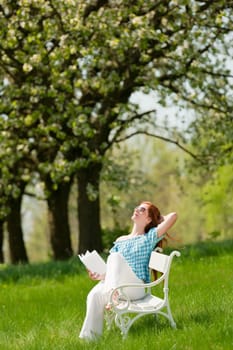Red hair woman sitting on white bench in green meadow, shallow DOF