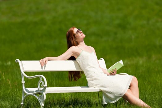 Red hair woman relaxing with book on white bench in a meadow shallow DOF