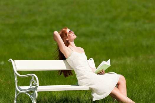 Red hair woman enjoying sun on white bench in a meadow shallow DOF