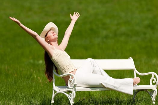 Red hair woman enjoying sun on white bench in a meadow shallow DOF