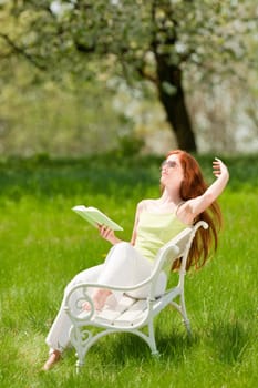 Red hair woman sitting on white bench in green meadow, shallow DOF