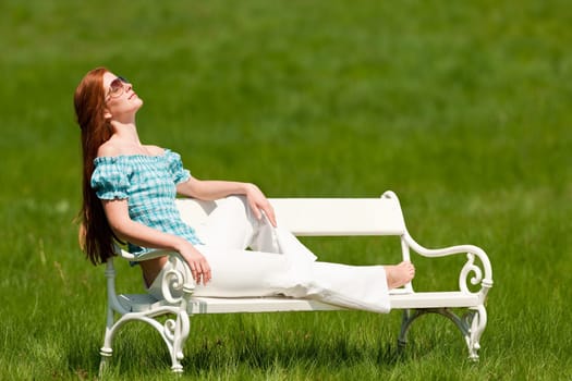 Red hair woman enjoying sun on white bench in a meadow shallow DOF