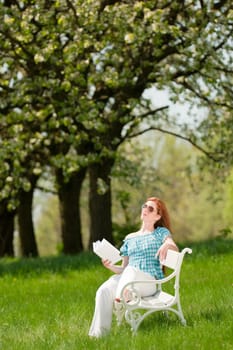 Red hair woman reading book on white bench in a meadow shallow DOF