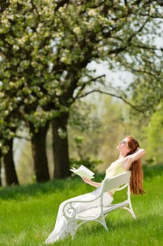 Red hair woman relaxing on white bench in a meadow shallow DOF