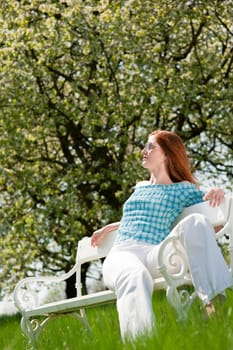 Red hair woman enjoying sun on white bench in a meadow shallow DOF