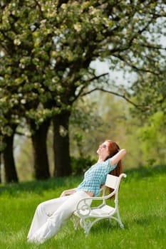 Red hair woman relaxing on white bench in a meadow shallow DOF