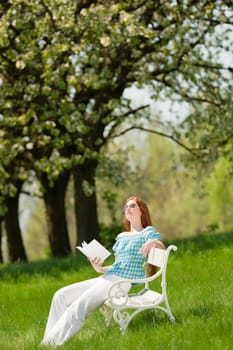Red hair woman reading book on white bench in a meadow shallow DOF
