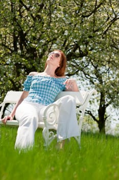 Red hair woman enjoying spring sun on white bench in a meadow shallow DOF