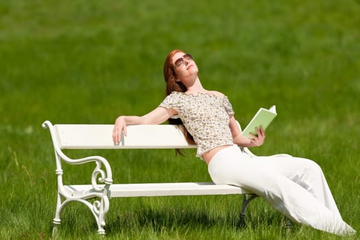 Red hair woman enjoying sun on white bench in a meadow shallow DOF