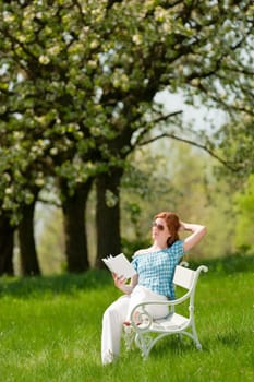 Red hair woman reading white book on a bench in a meadow shallow DOF