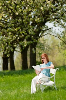 Red hair woman reading book on white bench in a meadow shallow DOF