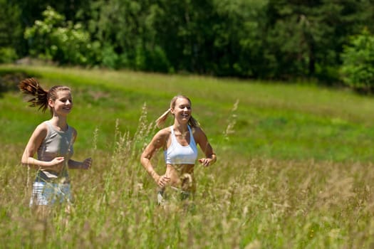 Two young woman jogging in a meadow on sunny day