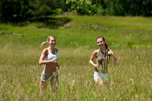 Two young woman jogging in a meadow on sunny day