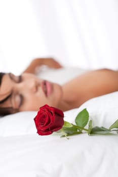 Woman lying in white bed, focus on rose, shallow DOF
