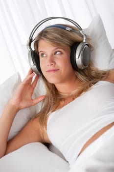 Young smiling woman listening to music with headphones on white sofa