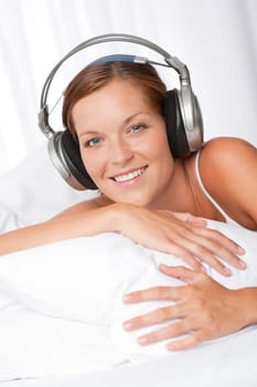 Young woman in white with headphones listening to music in bed
