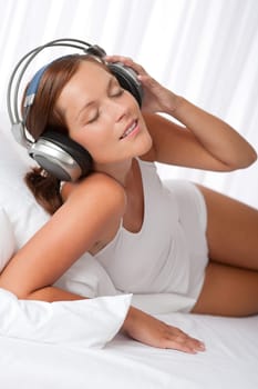 Young woman in white with headphones listening to music in bedroom