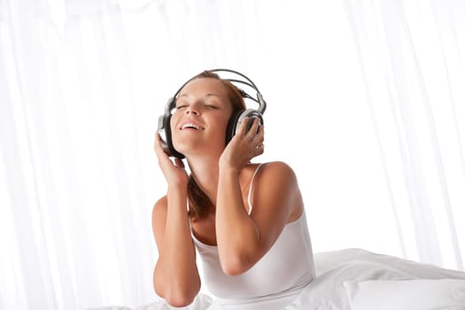 Young woman in white with headphones listening to music in bedroom