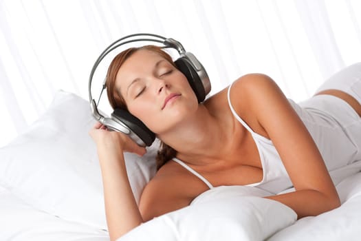 Young woman in white with headphones listening to music in bedroom
