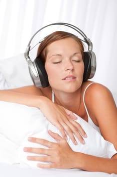 Young woman in white with headphones listening to music in bedroom