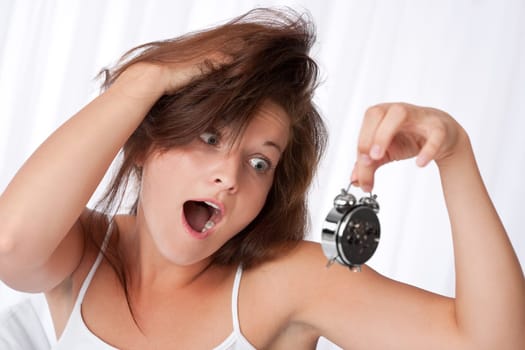 Surprised woman watching alarm clock in white bedroom