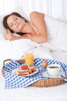 Woman sleeping in white bed, homemade breakfast in foreground