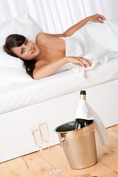 Naked woman in white bed with champagne and two glasses