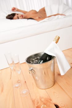 Bottle of champagne in ice bucket, naked woman in background
