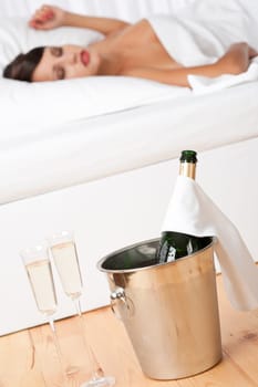 Champagne in ice bucket and two glasses, woman sleeping in background