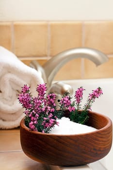 Pretty heather flowers in a bowl of Epsom salts on a bath tub edge ready to bathe.