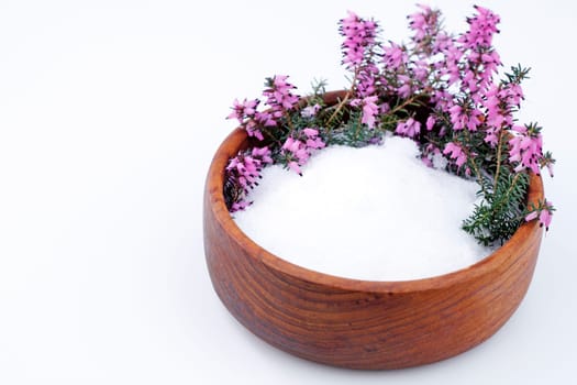 Beautiful purple heather flowers and white Epsom salts wait in a teak wood bowl on a white background.