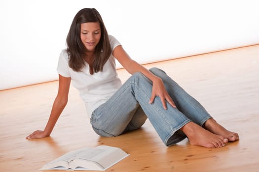 Happy teenager sitting with book on wooden floor