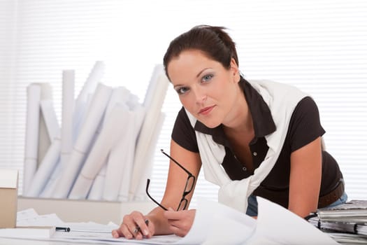 Young female architect with plans at the office holding glasses