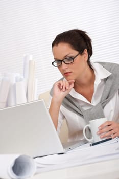 Female architect with laptop and coffee sitting at the office