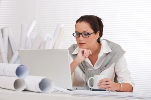 Female architect with laptop and coffee sitting at the office
