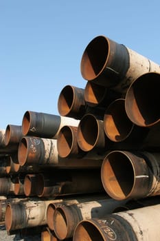 Pile of large industrial steel pipes rusting under clear blue sky