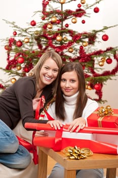 Two women packing Christmas present in front of tree