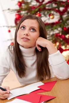Young woman writing Christmas card in front of tree