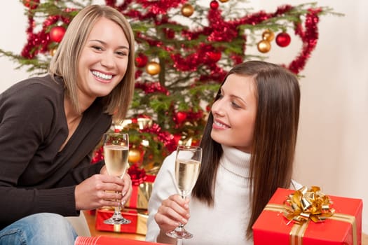 Two young woman with champagne and Christmas tree and present