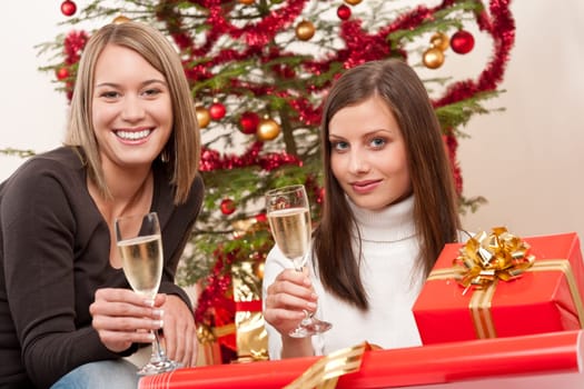 Two young woman with champagne and Christmas tree and present