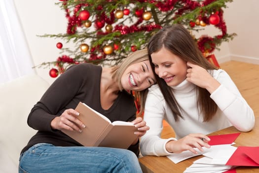 Two young women writing Christmas cards in front of tree